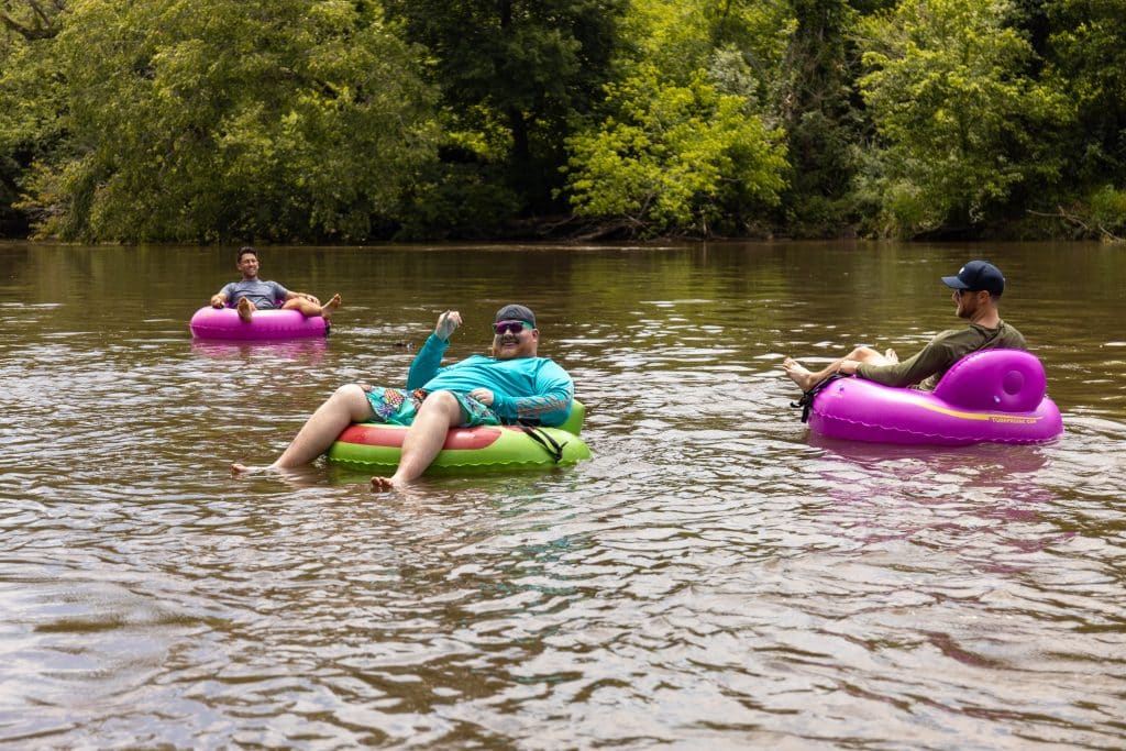 Guys enjoying their asheville tubing adventure in pink and green tubes wearing sunglasses surrounded by nature