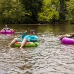 Guys enjoying their asheville tubing adventure in pink and green tubes wearing sunglasses surrounded by nature