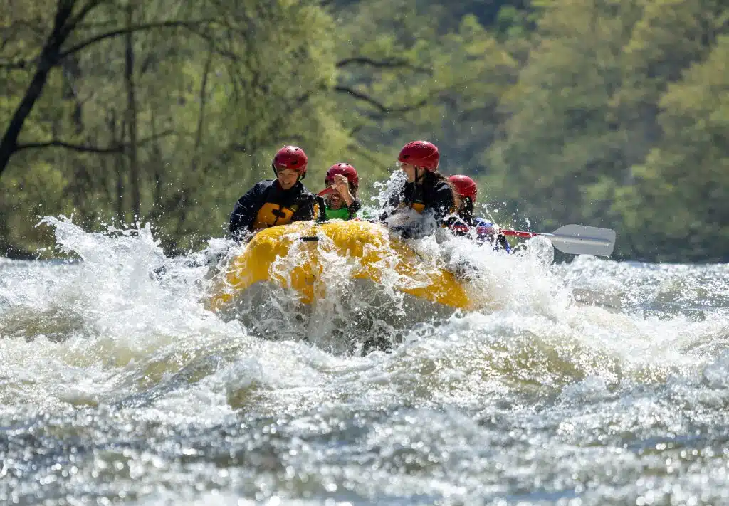 Kids getting splashed in the bow of a yellow raft having fun on the river