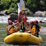 Rafters celebrating a successful rafting trip down Section 9 of the French Broad River just outside of Asheville North Carolina. They are smiling and raising their paddles in the air wearing life jackets and helmets.